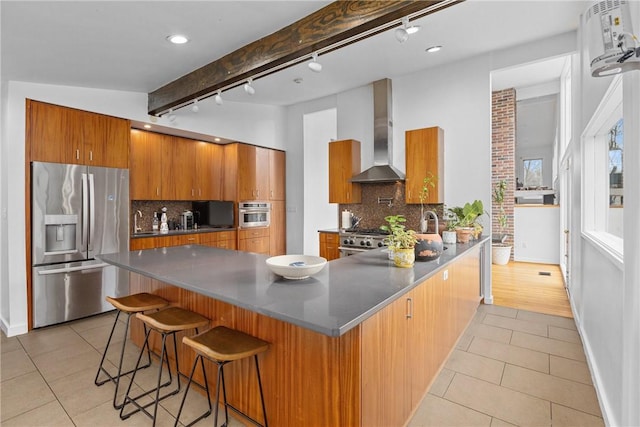 kitchen featuring light tile patterned flooring, beamed ceiling, a kitchen bar, stainless steel appliances, and wall chimney exhaust hood