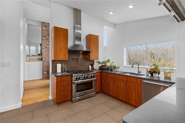 kitchen featuring sink, light tile patterned floors, appliances with stainless steel finishes, tasteful backsplash, and wall chimney exhaust hood