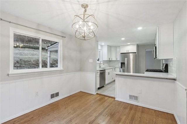 kitchen with decorative light fixtures, tasteful backsplash, white cabinetry, light hardwood / wood-style floors, and stainless steel appliances