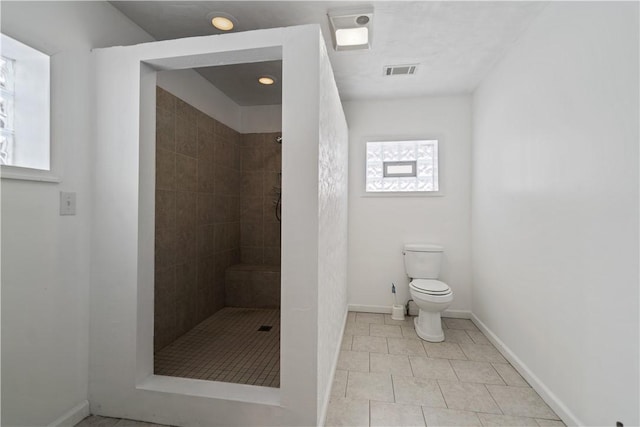 bathroom featuring tile patterned flooring, toilet, and tiled shower