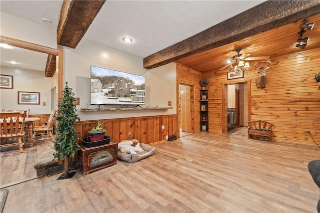 living room with ceiling fan, light hardwood / wood-style flooring, beamed ceiling, and wood walls