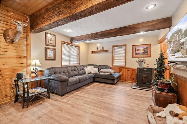 living room featuring beamed ceiling, a wood stove, wooden walls, and light hardwood / wood-style flooring