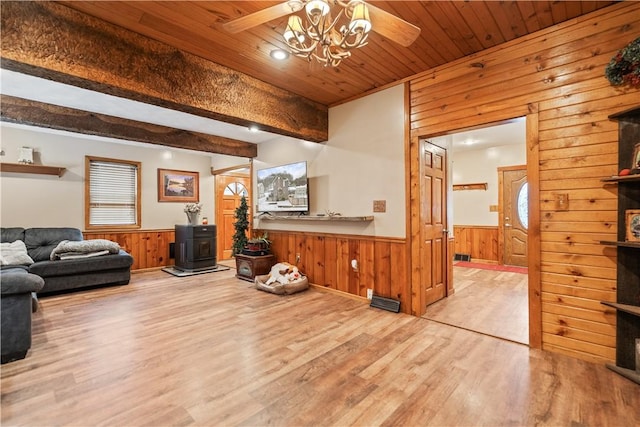 living room with wooden ceiling, a wood stove, wooden walls, beamed ceiling, and light hardwood / wood-style floors