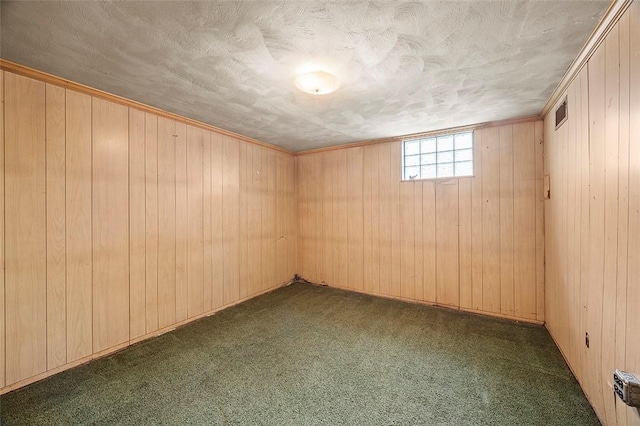 spare room featuring dark carpet, a textured ceiling, and wood walls