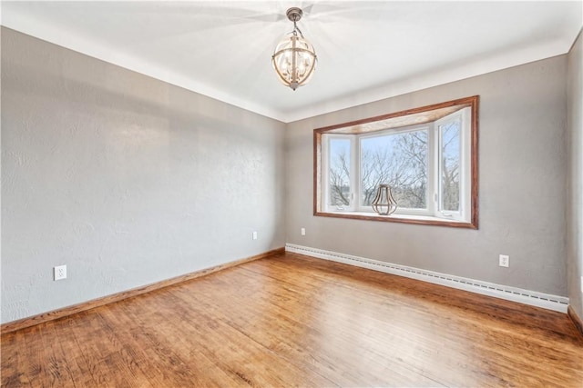 empty room featuring hardwood / wood-style flooring, an inviting chandelier, and a baseboard heating unit