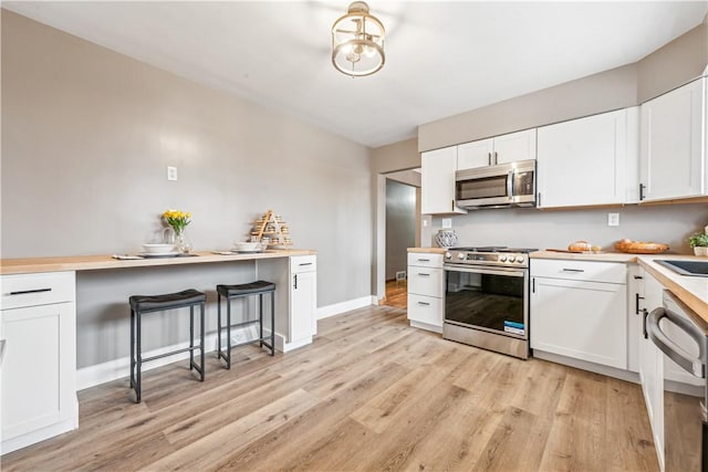 kitchen with white cabinetry, sink, a breakfast bar area, stainless steel appliances, and light wood-type flooring