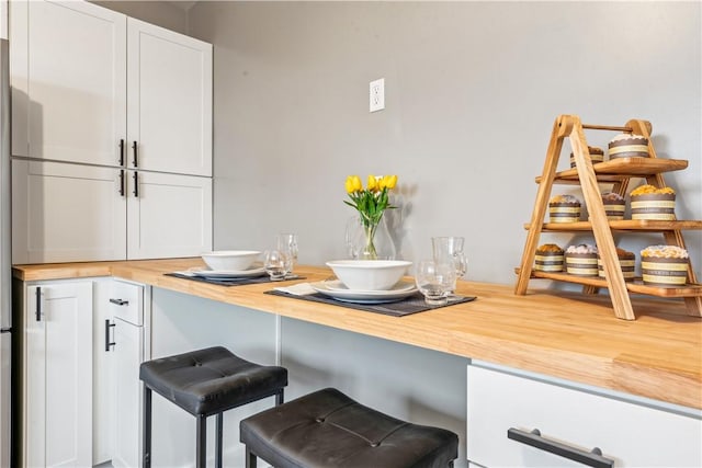 kitchen with butcher block counters, white cabinetry, and a kitchen bar