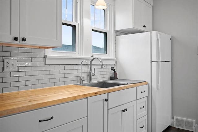 kitchen featuring sink, butcher block countertops, white cabinetry, backsplash, and white refrigerator