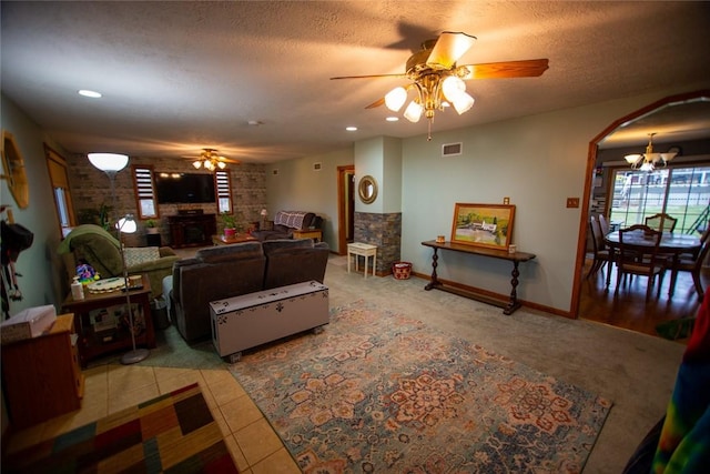 living room with ceiling fan with notable chandelier, a fireplace, a textured ceiling, and light tile patterned flooring