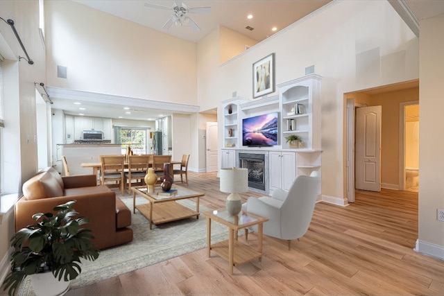 living room with ceiling fan, a towering ceiling, and light hardwood / wood-style floors