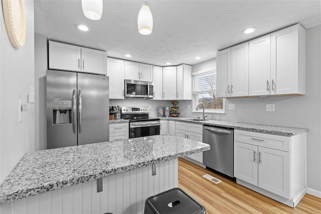 kitchen with appliances with stainless steel finishes, a breakfast bar, pendant lighting, sink, and white cabinets