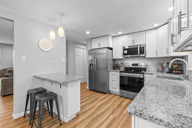 kitchen featuring a breakfast bar, pendant lighting, white cabinetry, sink, and stainless steel appliances