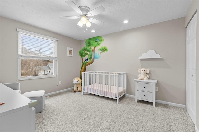 carpeted bedroom with ceiling fan, a nursery area, a textured ceiling, and a closet