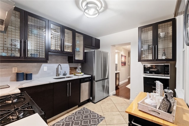 kitchen with tasteful backsplash, stainless steel appliances, light stone countertops, light tile patterned floors, and sink