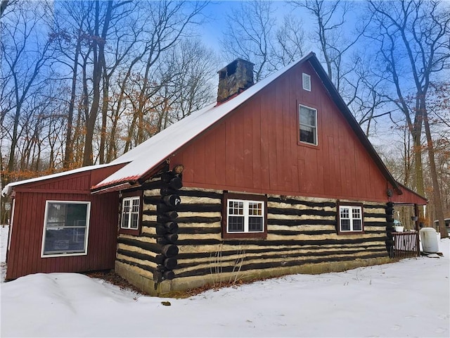 snow covered property featuring log siding and a chimney