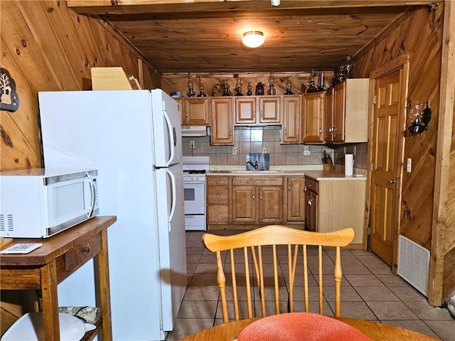 kitchen featuring white appliances, light tile patterned floors, under cabinet range hood, and a sink