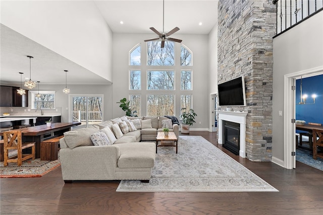 living room featuring a towering ceiling, ceiling fan with notable chandelier, a fireplace, sink, and dark wood-type flooring