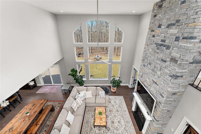 living room featuring dark wood-type flooring, plenty of natural light, a stone fireplace, and a high ceiling