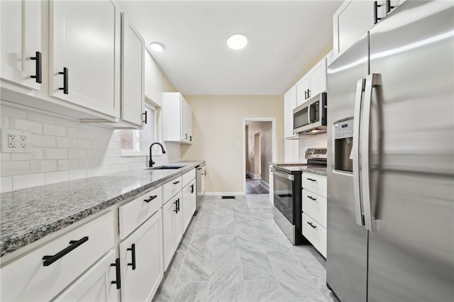 kitchen with sink, white cabinetry, tasteful backsplash, light stone counters, and stainless steel appliances