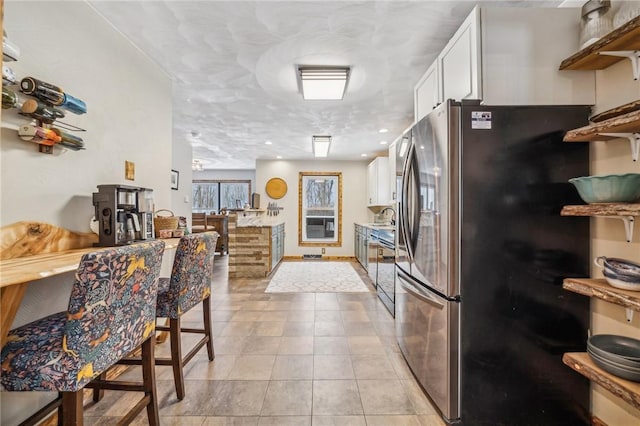 kitchen with dishwasher, sink, stainless steel fridge, white cabinets, and light tile patterned floors