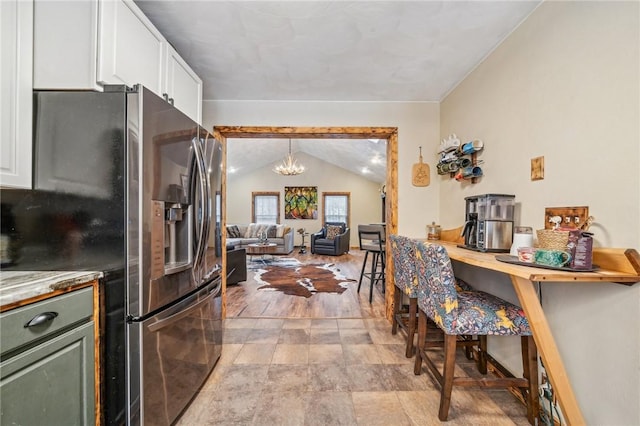 kitchen with stainless steel fridge, white cabinetry, hanging light fixtures, a notable chandelier, and vaulted ceiling