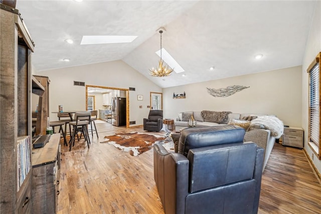 living room with wood-type flooring, lofted ceiling with skylight, and a notable chandelier