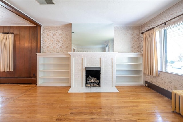 unfurnished living room featuring baseboard heating, radiator, a brick fireplace, and light wood-type flooring