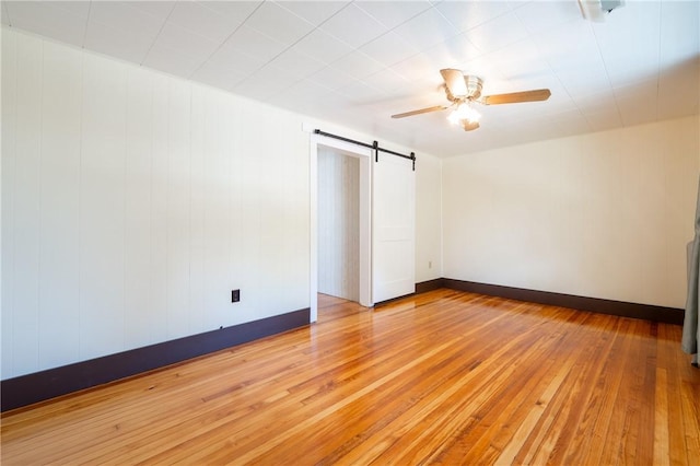 spare room with ceiling fan, a barn door, and light wood-type flooring