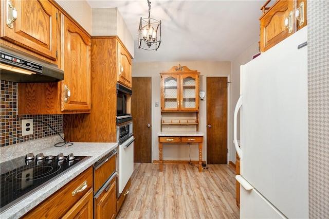 kitchen with black appliances, a chandelier, hanging light fixtures, light wood-type flooring, and backsplash