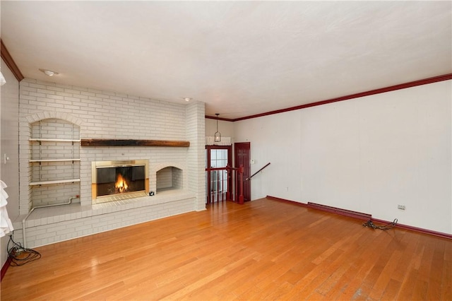 unfurnished living room featuring a brick fireplace, crown molding, and wood-type flooring