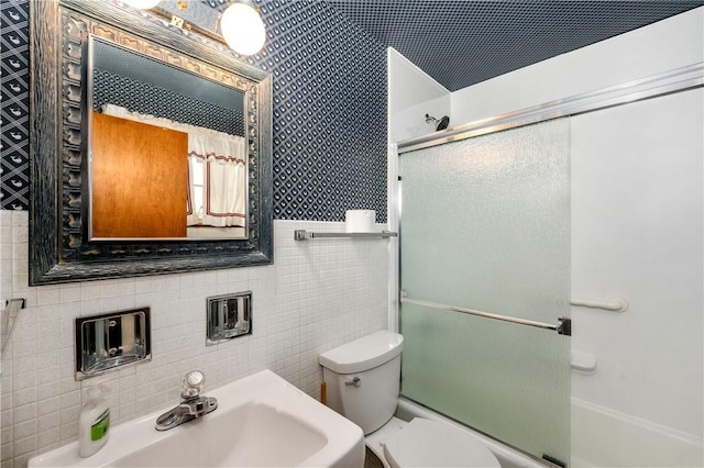 full bathroom with bath / shower combo with glass door, sink, tile walls, and toilet