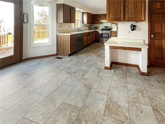 kitchen with baseboards, a sink, light countertops, appliances with stainless steel finishes, and under cabinet range hood