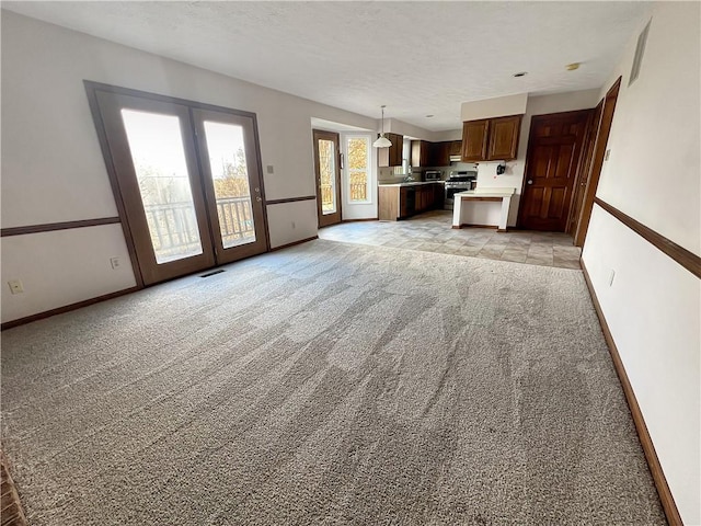 unfurnished living room with baseboards, french doors, a textured ceiling, visible vents, and light colored carpet