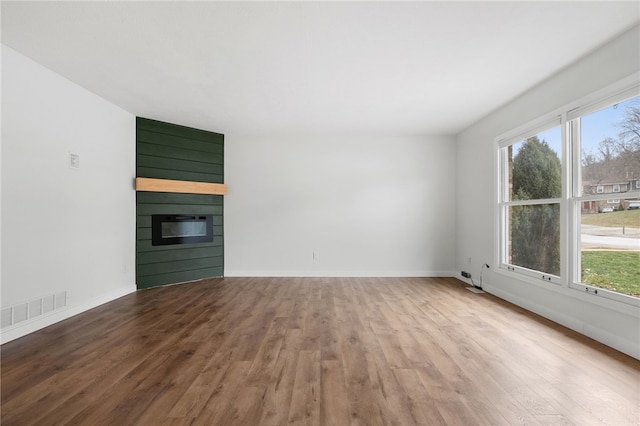 unfurnished living room featuring a healthy amount of sunlight, a large fireplace, and hardwood / wood-style floors