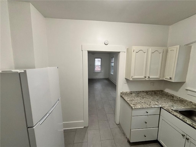 kitchen with white cabinetry, sink, and white fridge