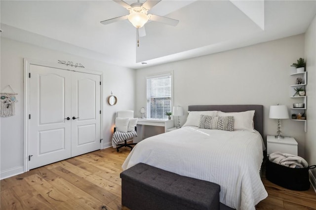 bedroom with a closet, ceiling fan, light wood-type flooring, and a tray ceiling