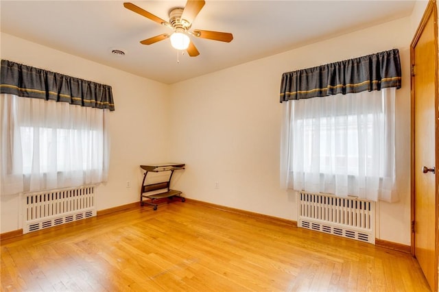 empty room with wood-type flooring, radiator heating unit, and a healthy amount of sunlight