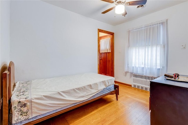 bedroom with ceiling fan, radiator heating unit, and wood-type flooring