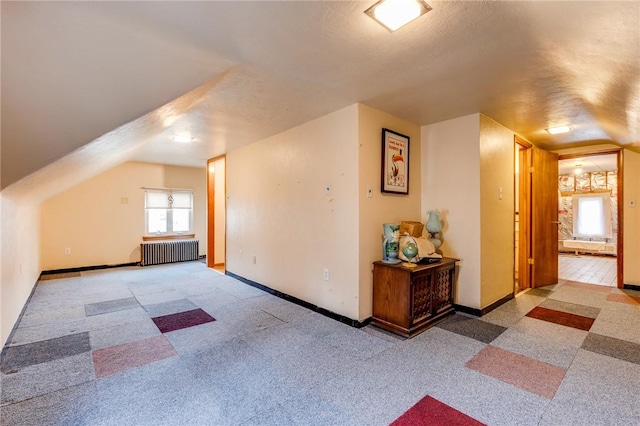 additional living space featuring vaulted ceiling, radiator heating unit, light colored carpet, and a textured ceiling