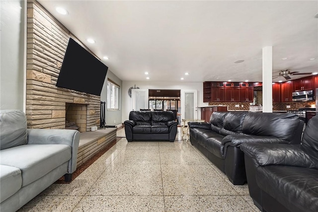 living room with a stone fireplace and ceiling fan