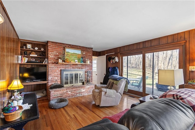 living room featuring a fireplace, built in shelves, wood-type flooring, and wood walls