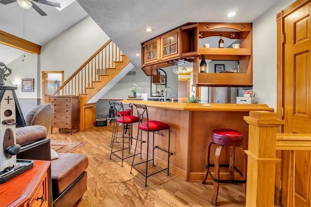 bar with lofted ceiling, sink, ceiling fan, a textured ceiling, and light hardwood / wood-style flooring