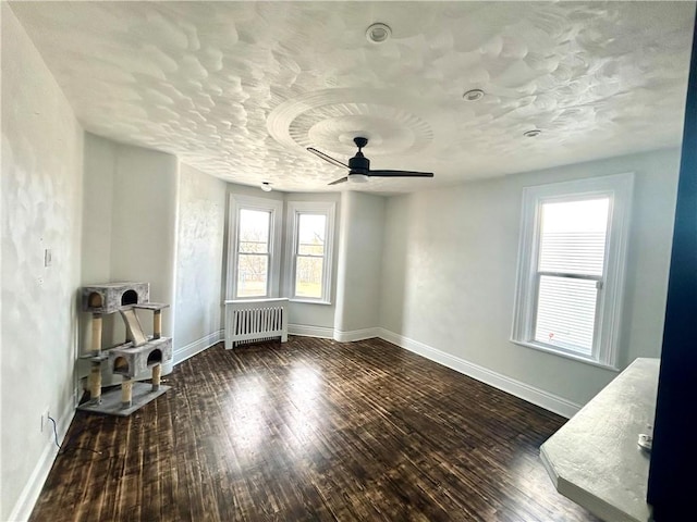 empty room featuring dark hardwood / wood-style flooring, radiator heating unit, and ceiling fan