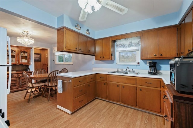 kitchen with sink, ceiling fan with notable chandelier, light hardwood / wood-style floors, decorative light fixtures, and kitchen peninsula