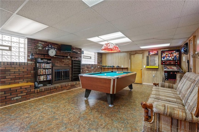 rec room featuring a paneled ceiling, brick wall, and a brick fireplace