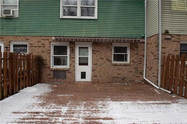 snow covered property entrance with a wooden deck and cooling unit