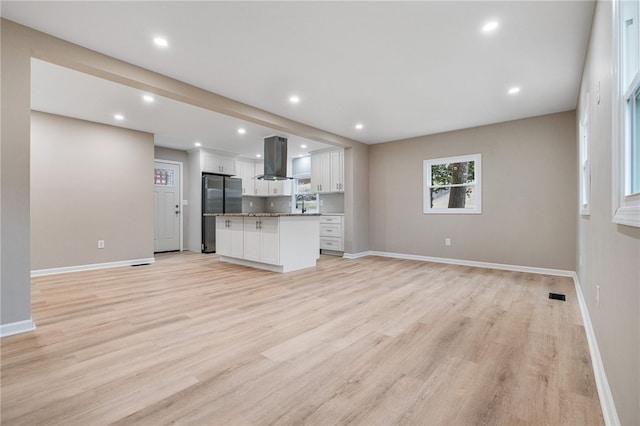 kitchen featuring range hood, white cabinetry, stainless steel fridge, a center island, and light hardwood / wood-style floors