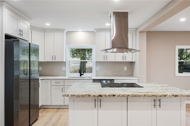 kitchen featuring stainless steel appliances, light stone countertops, island range hood, and white cabinets