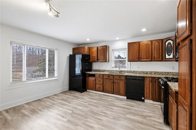 kitchen with light stone countertops, black appliances, light wood-type flooring, and a sink