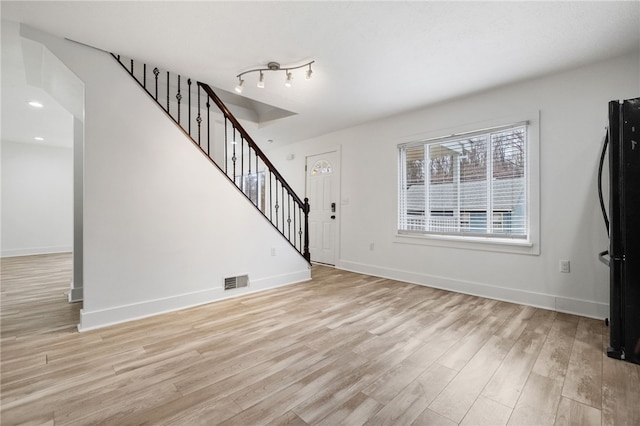 unfurnished living room featuring stairway, visible vents, light wood-style flooring, and baseboards